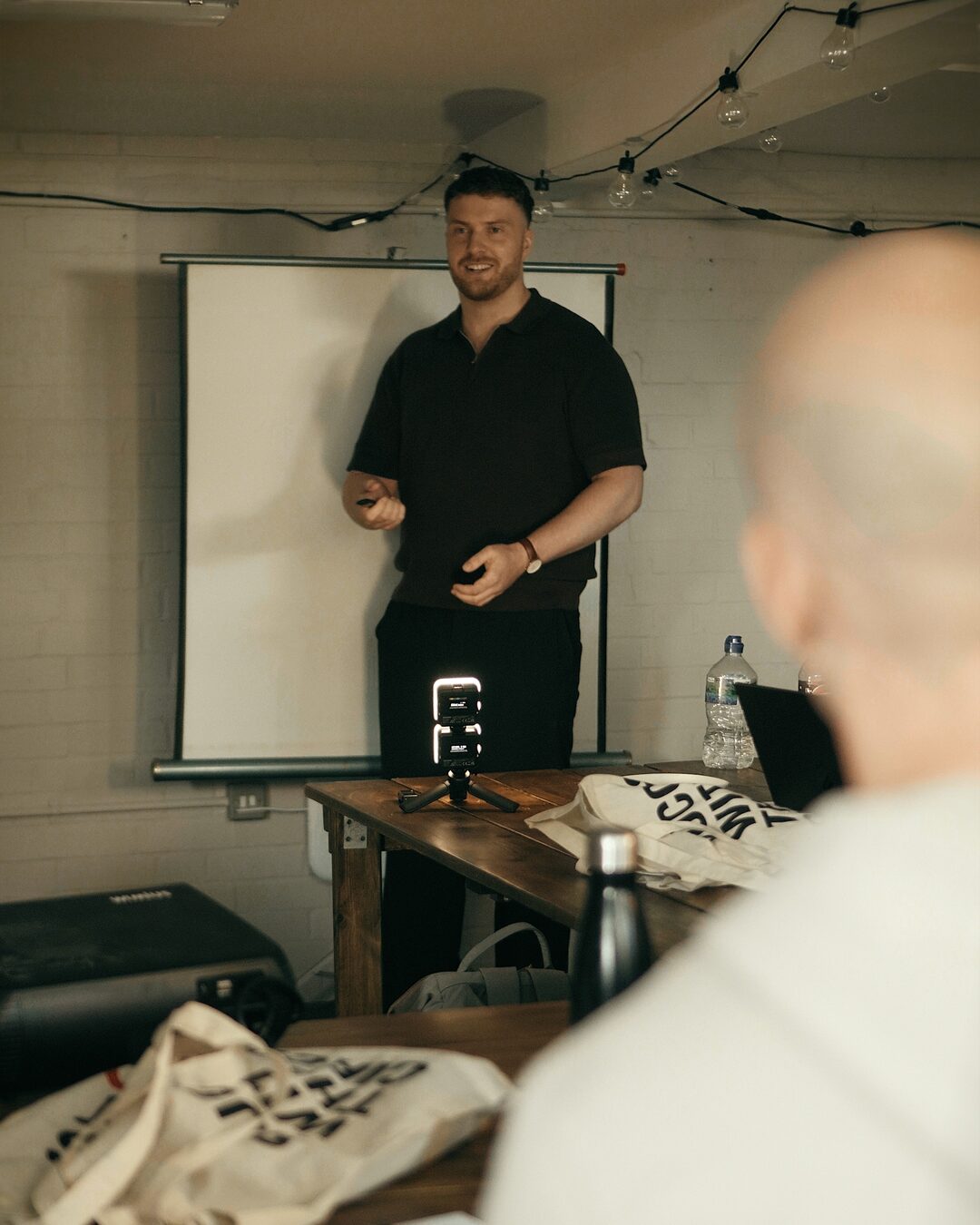 Charlie Beestone mid-talk, gesturing in front of a presentation screen